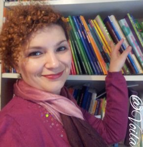 Young woman, smiling, in front of a bookshelf